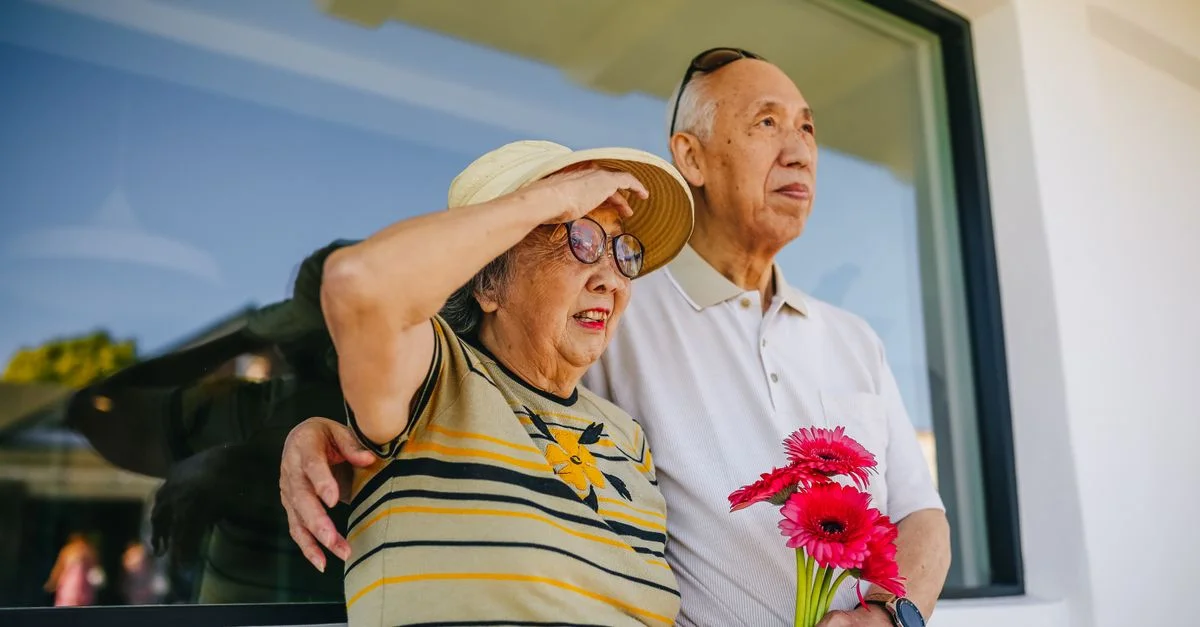 Couple senior se tenant à l'extérieur, tenant des fleurs, profitant d'une journée ensoleillée ensemble.