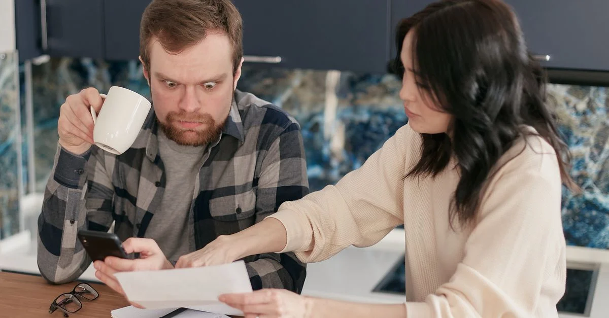 Un couple examine des factures ménagères dans une cuisine, semblant préoccupé et concentré.