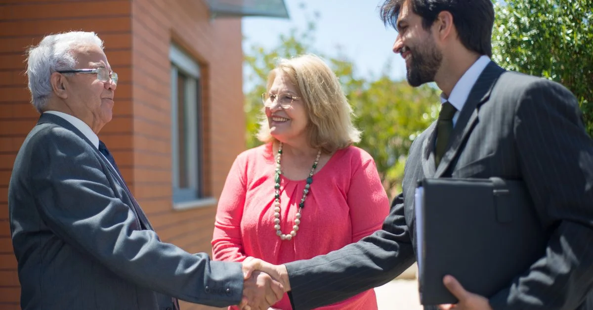 Agent immobilier et couple mature se serrant la main en plein air, scellant un accord avec des sourires.