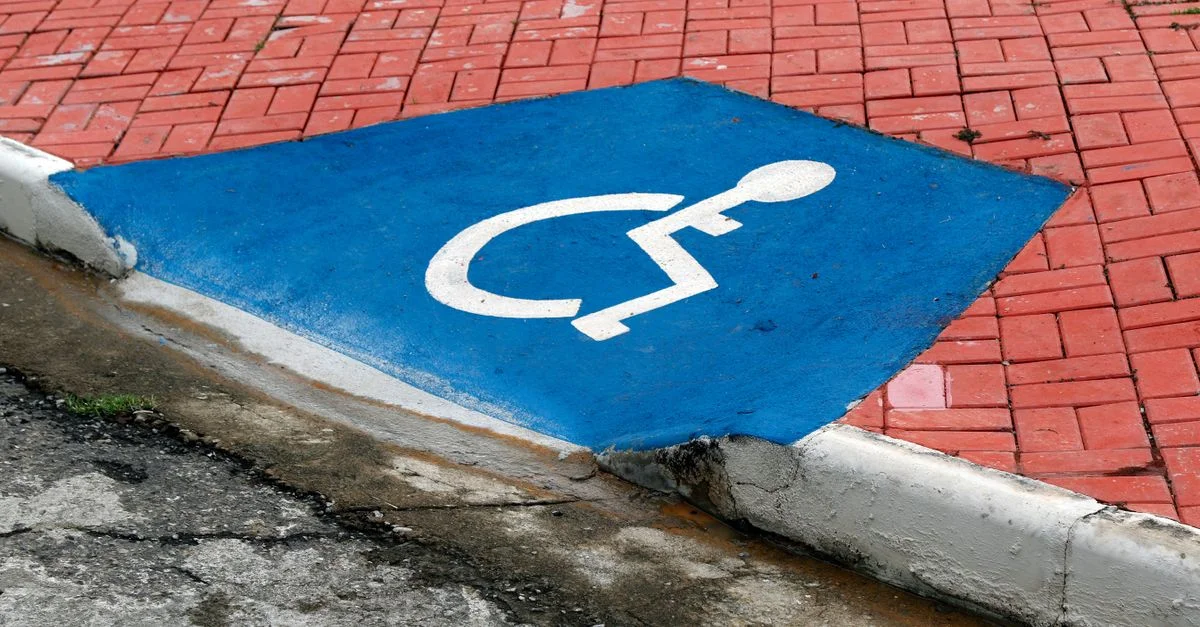 Gros plan d'un symbole de stationnement pour handicapés bleu sur un pavé en briques rouges.