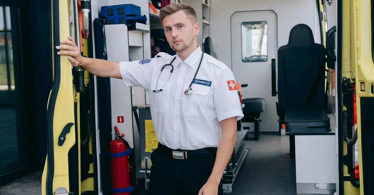 Paramédic masculin se tenant à côté des portes ouvertes de l'ambulance, prêt à intervenir en cas d'urgence.