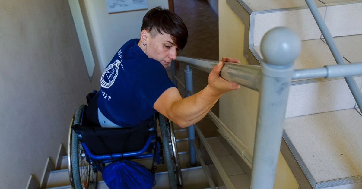 Un individu déterminé en fauteuil roulant sur des escaliers, utilisant une main courante pour se soutenir.