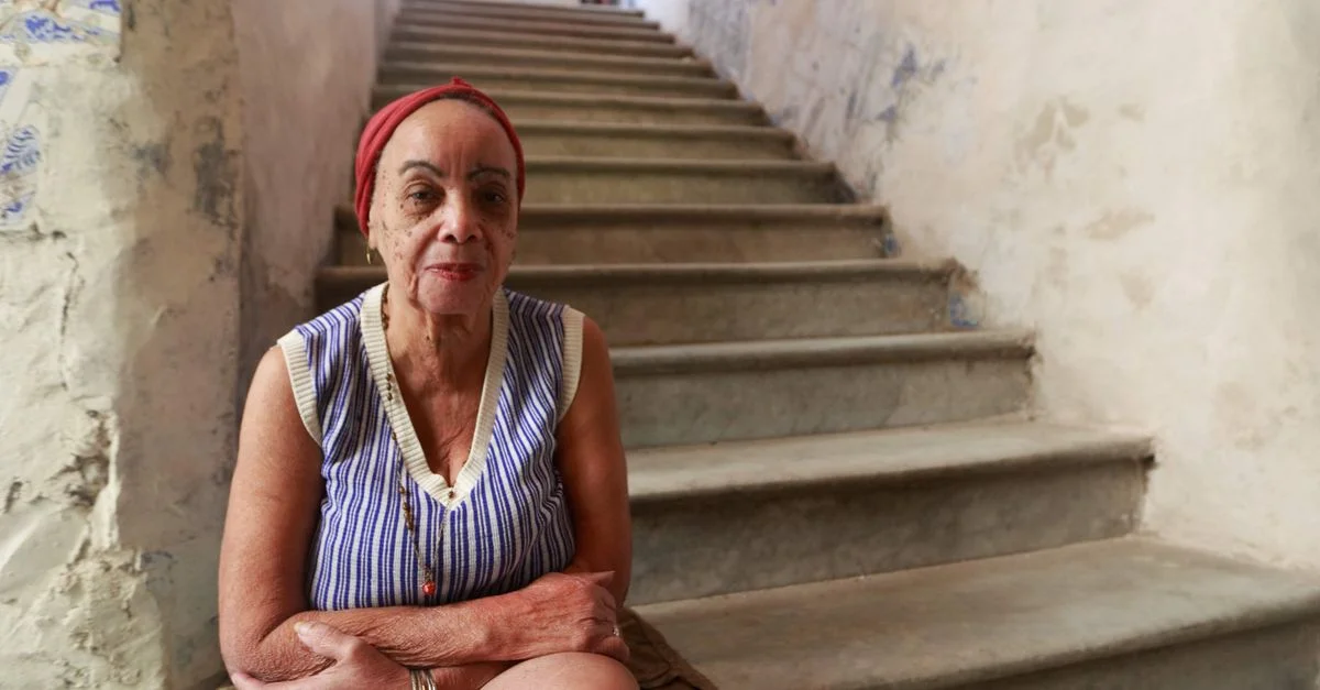 Portrait d'une femme senior assise sur des escaliers en béton rustiques à l'intérieur, montrant détermination et élégance.