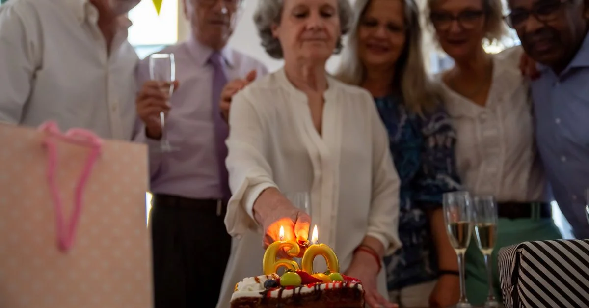 Groupe de personnes âgées célébrant un anniversaire à l'intérieur avec un gâteau et du champagne.