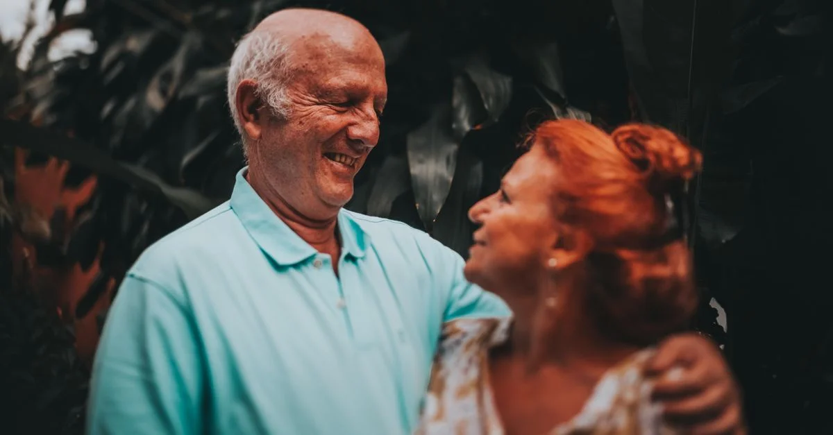 Couple âgé souriant et s'enlaçant dans un cadre extérieur luxuriant, capturant l'amour et l'amitié.