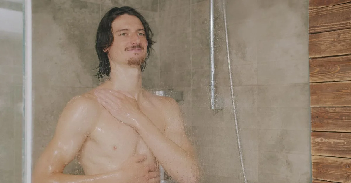 Un homme adulte prend une douche dans une salle de bains moderne carrelée de pierre naturelle.