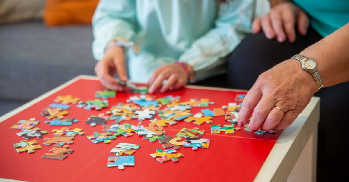 Gros plan sur des mains travaillant ensemble sur un puzzle coloré à l'intérieur, favorisant le travail d'équipe et la convivialité.