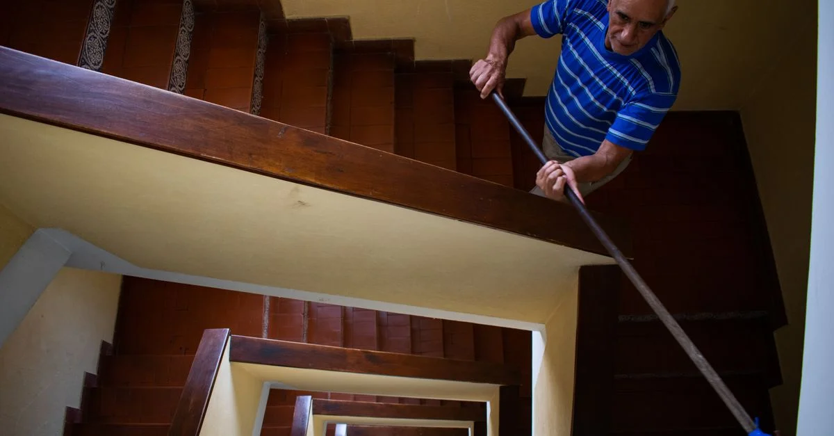 Un homme âgé nettoie un escalier intérieur avec une serpillère, illustrant la vie quotidienne et le travail.