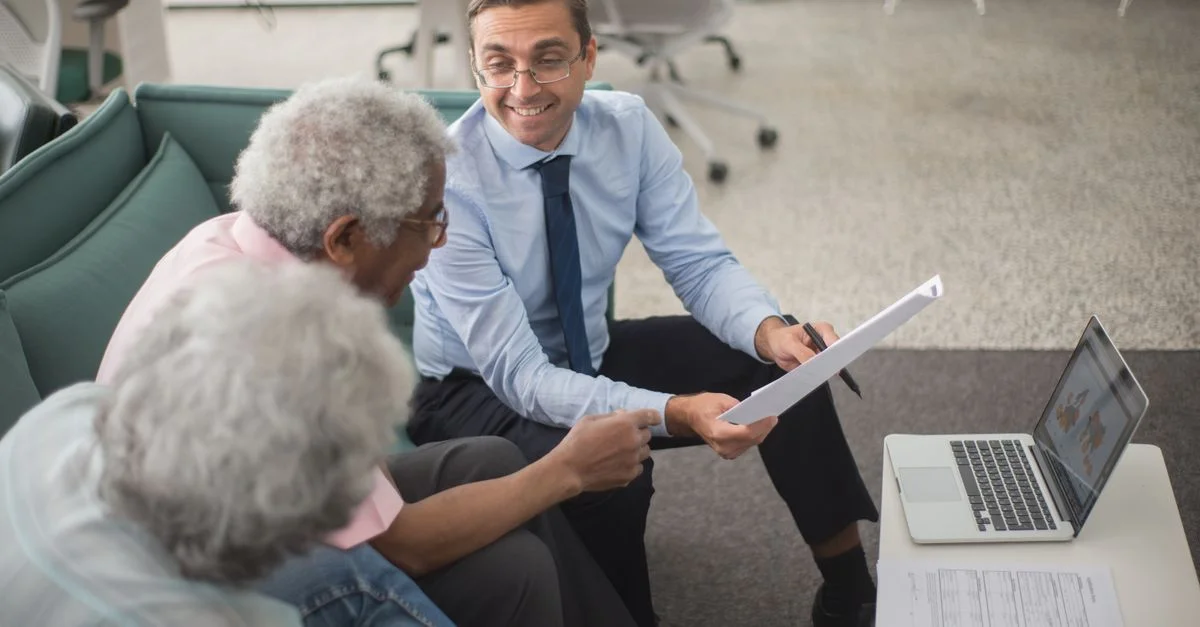 Consultant discutant des plans financiers avec des clients seniors dans un bureau moderne, utilisant des documents et un ordinateur portable.