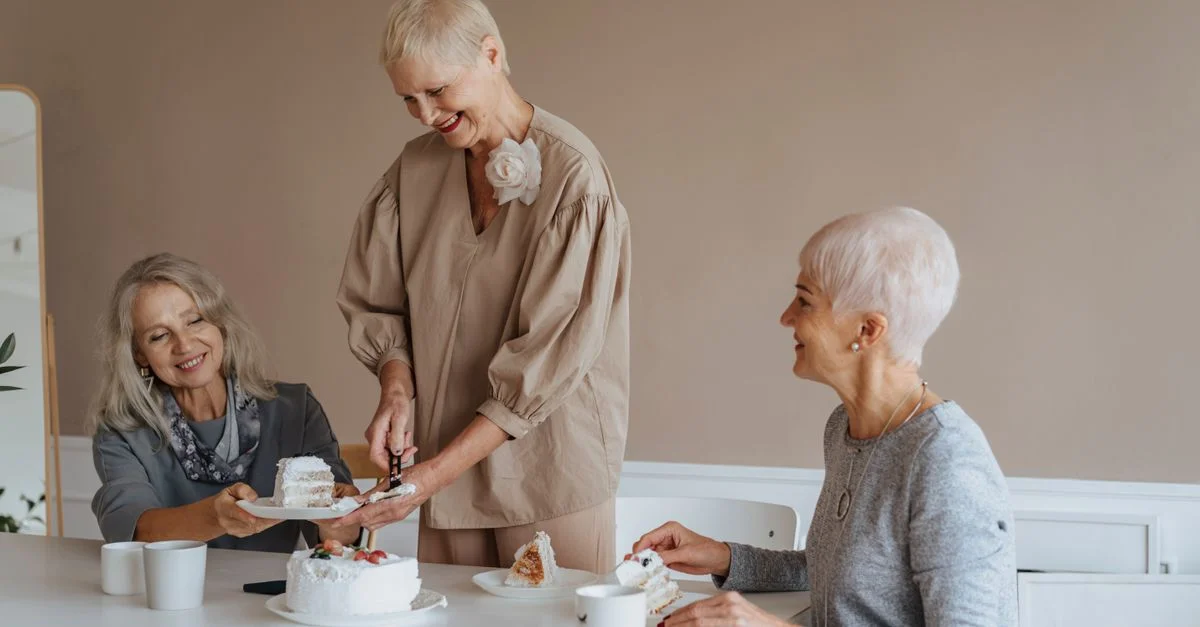 Trois femmes seniors profitant d'une célébration d'anniversaire avec un gâteau dans un cadre intérieur chaleureux.