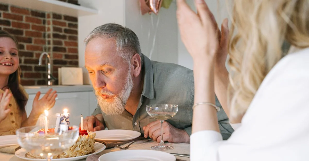 Un homme âgé célèbre son anniversaire en éteignant les bougies d'un gâteau dans un cadre intérieur chaleureux.