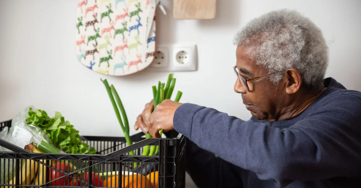 Un homme afro-américain senior organisant des légumes frais à l'intérieur, mettant en avant un mode de vie sain.