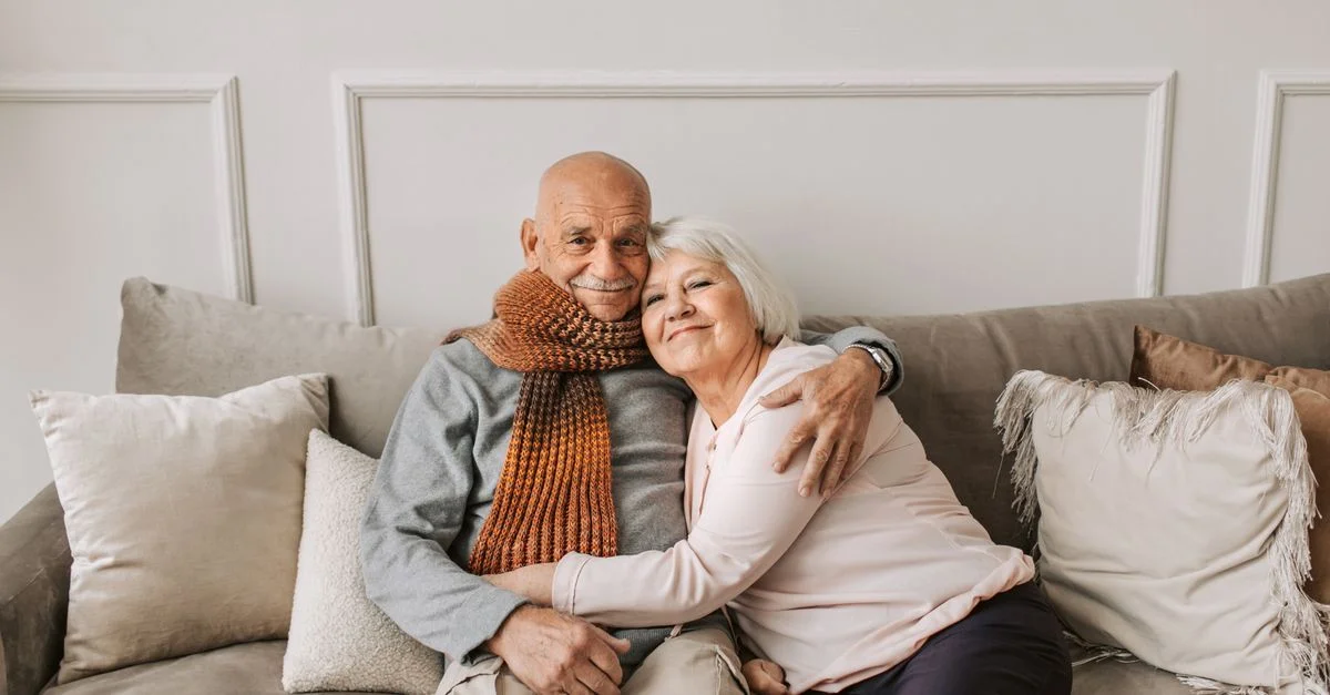 Un couple âgé affectueux s'enlaçant sur un canapé confortable à l'intérieur.