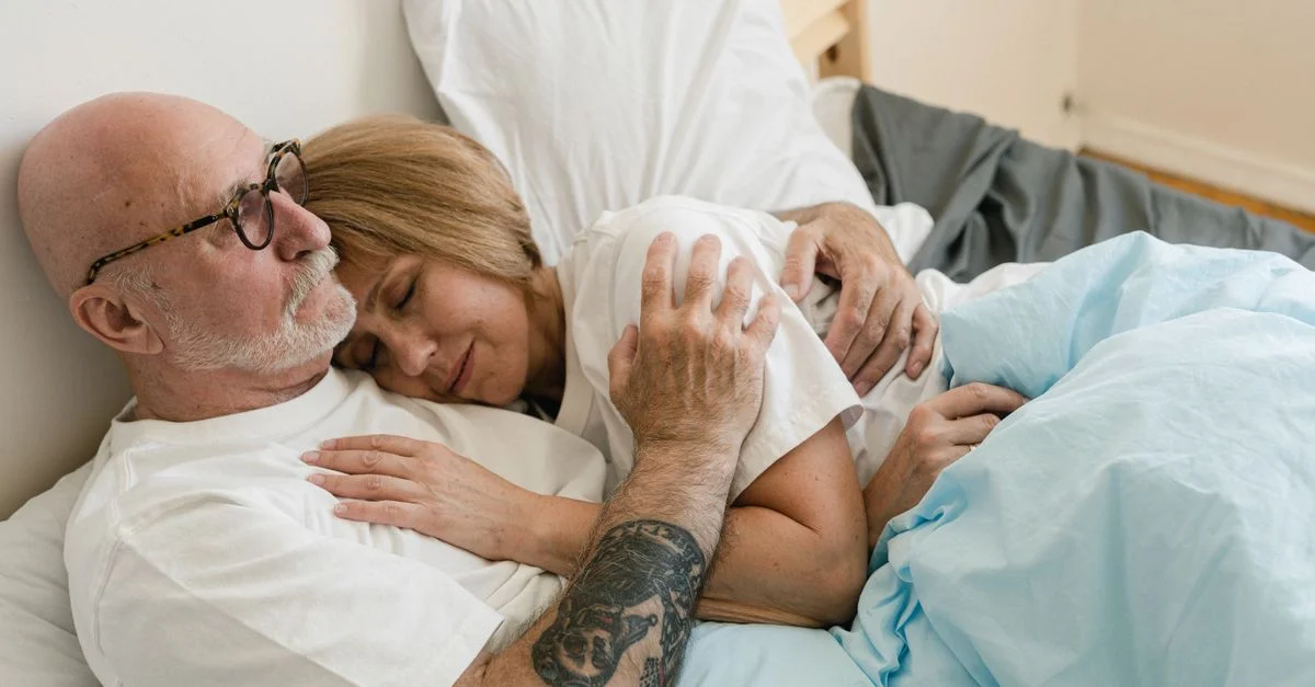 Couple senior s'étreignant au lit, montrant l'amour et la complicité.