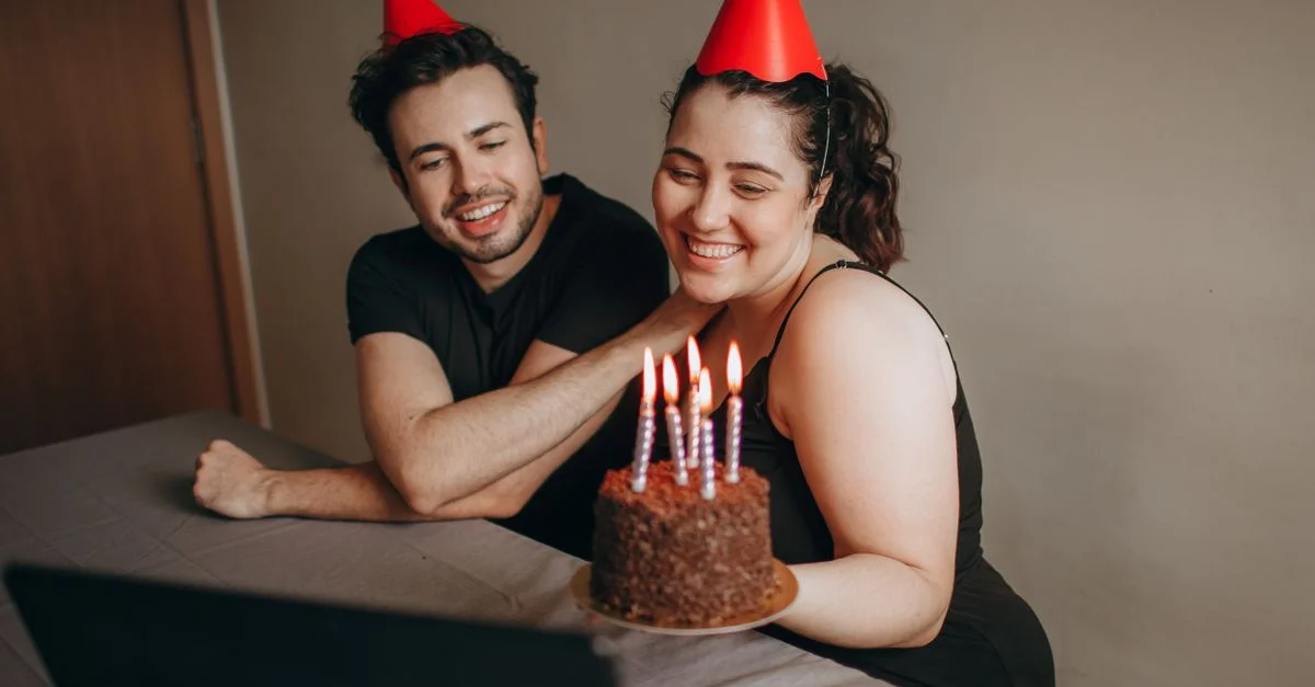 Deux adultes lors d'une célébration d'anniversaire virtuelle avec un gâteau et des chapeaux.