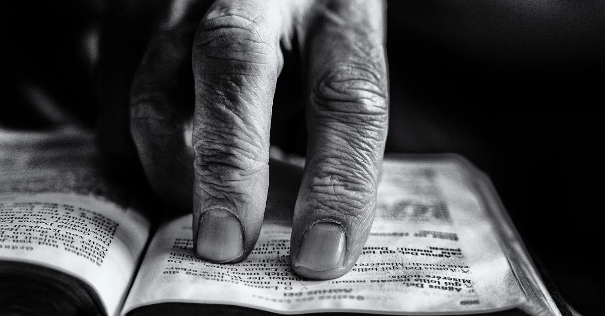Une image détaillée en noir et blanc d'une main âgée touchant les pages d'un livre ouvert.