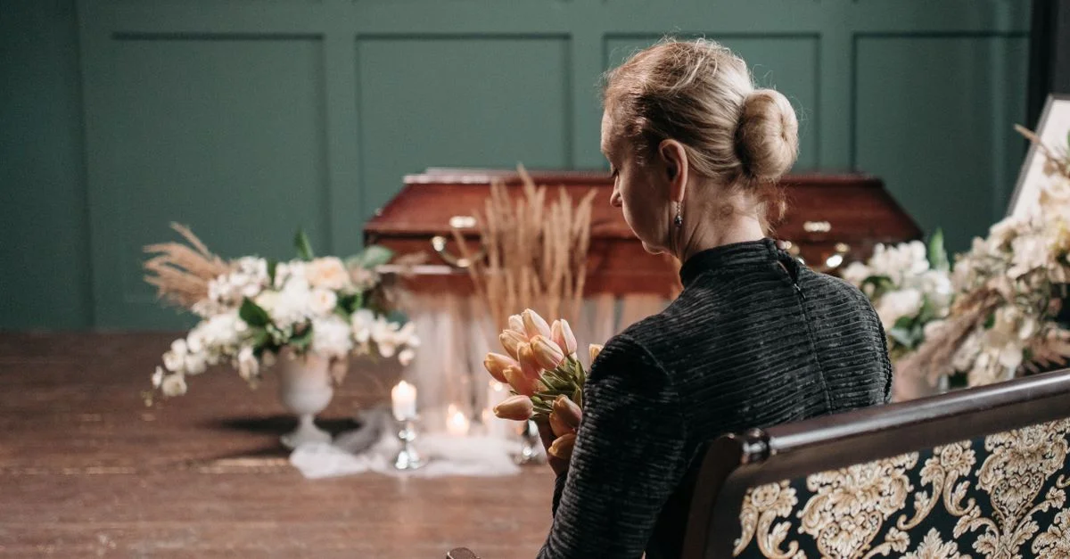 Une femme en deuil tenant des fleurs lors d'un enterrement, mettant en avant la tristesse et le souvenir.