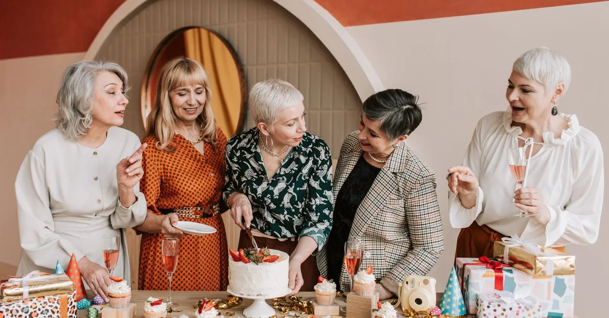 Des femmes seniors célèbrent joyeusement un anniversaire à l'intérieur avec un gâteau et des cadeaux.