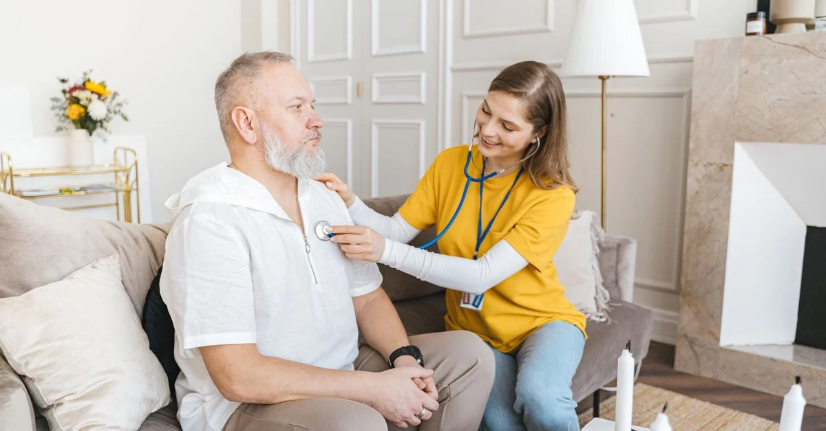 Une infirmière utilise un stéthoscope pour un contrôle à domicile sur un senior dans un salon confortable.