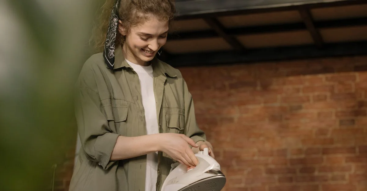 Une jeune femme avec des cheveux bouclés repasse des vêtements dans un intérieur moderne et confortable avec un mur en briques.