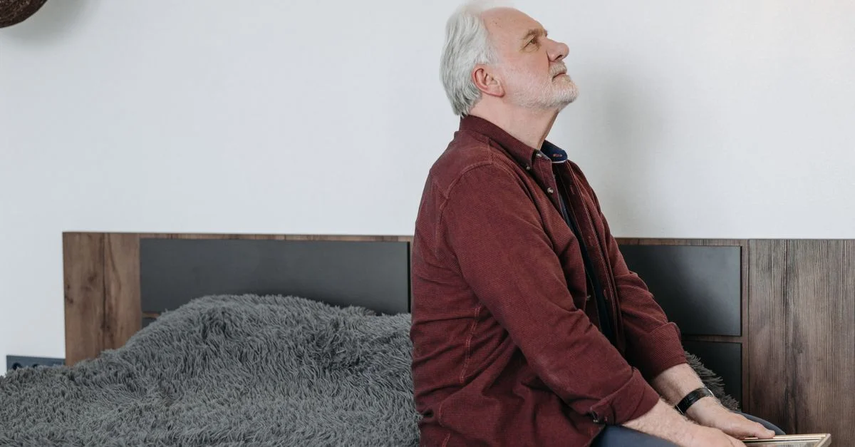 Homme senior assis sur le lit, tenant un cadre photo, perdu dans ses pensées et réflexions.