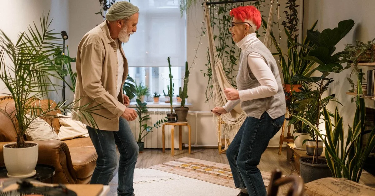 Un couple de seniors énergique dansant ensemble à la maison, entouré de plantes d'intérieur.