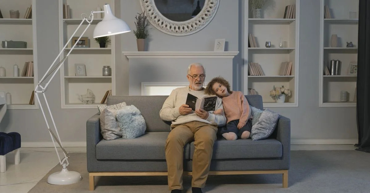 Une scène chaleureuse avec un grand-père lisant à sa petite-fille à la maison sur le canapé.