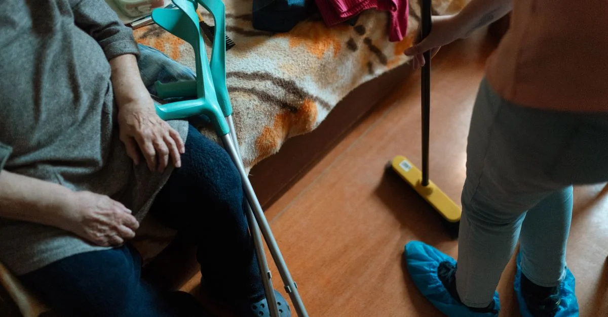Un soignant aide une femme âgée dans ses tâches de nettoyage, mettant en valeur le soutien aux soins à domicile.