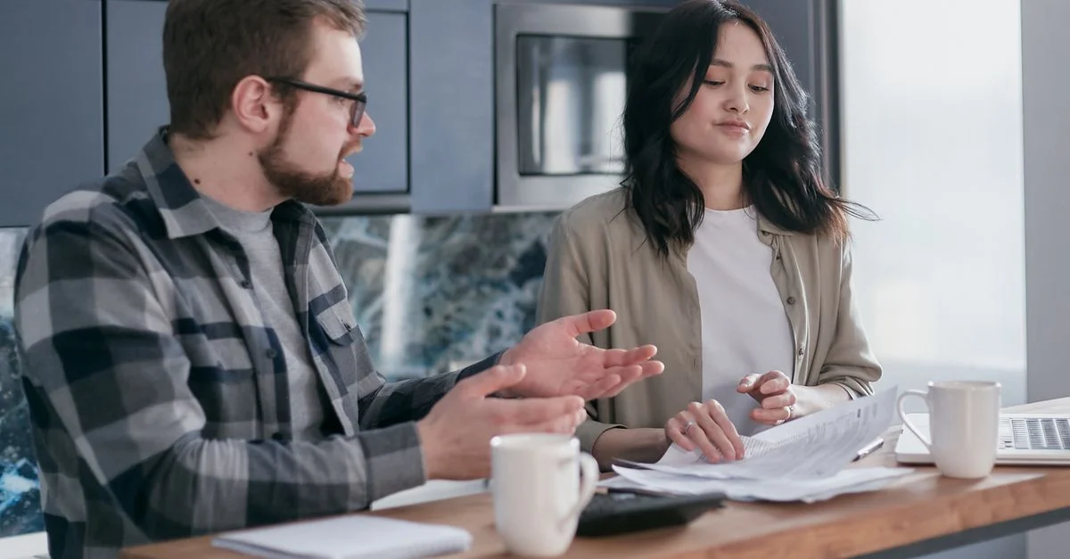 Un couple examinant des documents financiers dans leur cuisine, semblant concentré et inquiet.