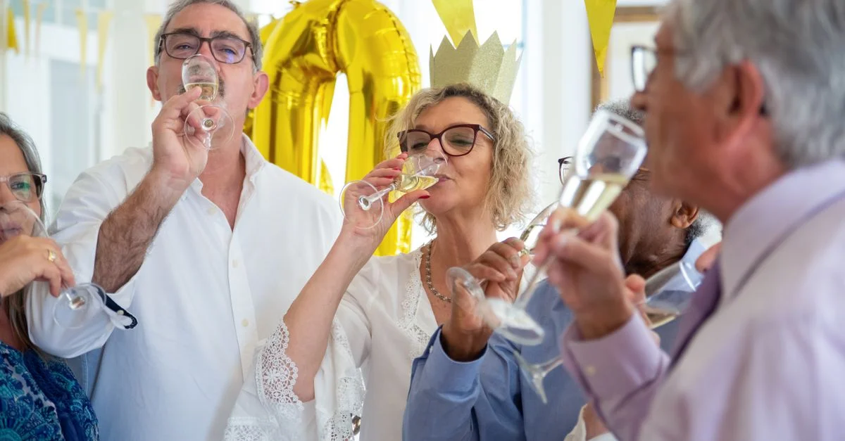 Un groupe joyeux de seniors célébrant un anniversaire à l'intérieur avec du champagne et des sourires.