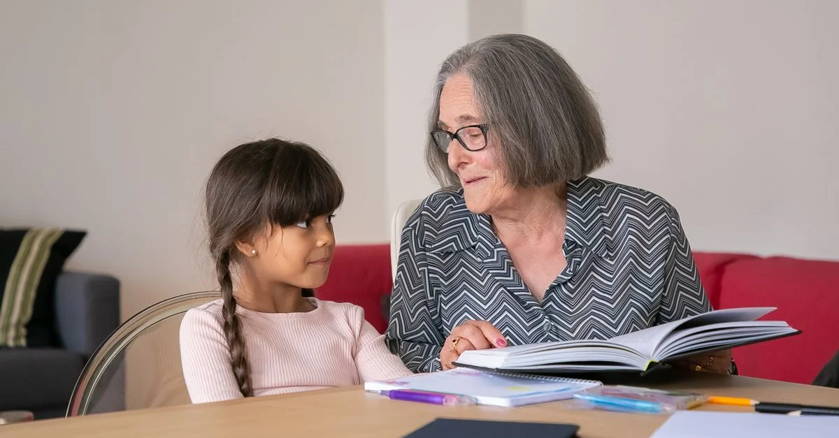 Une femme âgée et une jeune fille partageant un livre à l'intérieur, renforçant un lien grâce à la lecture.