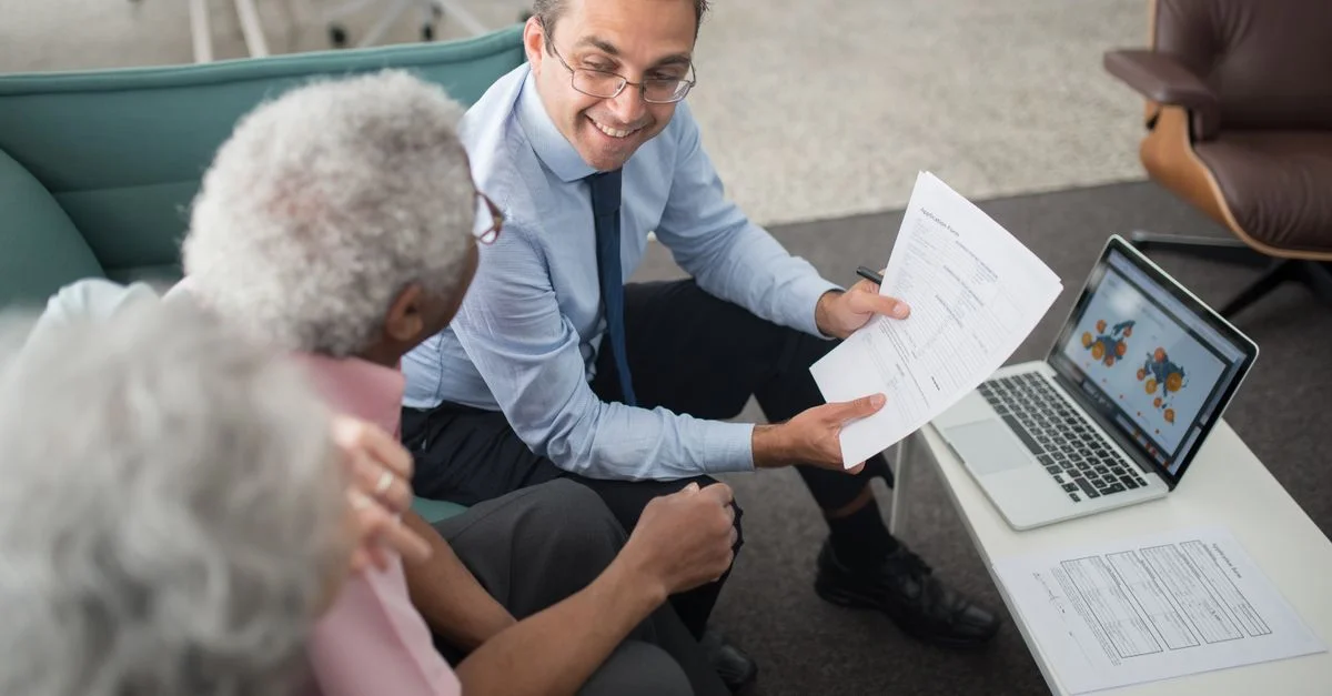Conseiller financier discutant de documents avec des clients seniors dans un cadre de bureau, mettant en avant une session de consultation collaborative.