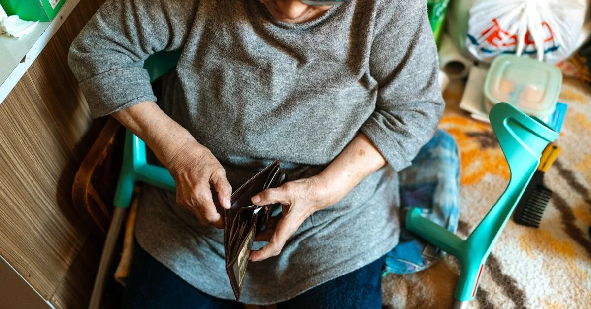 Femme âgée assise à l'intérieur gérant son portefeuille. Thème de soins à domicile.