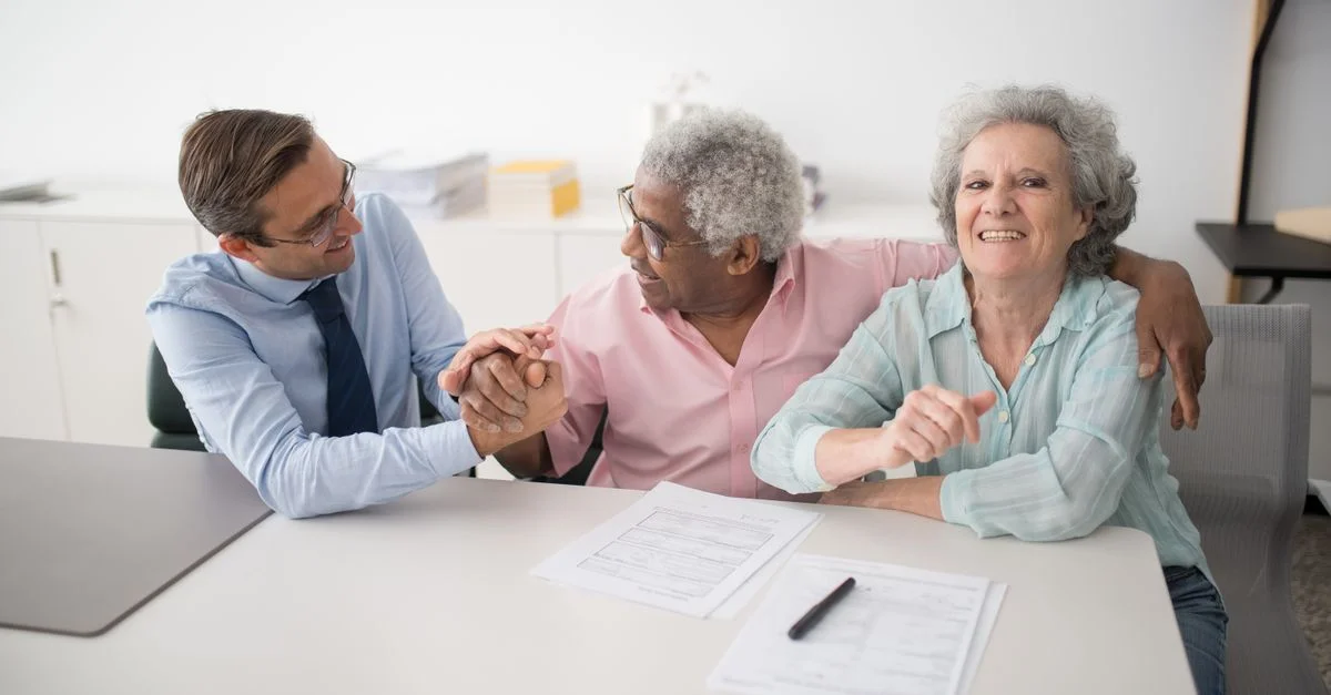 Couple senior en réunion de bureau avec un consultant, discutant de documents financiers et souriant.