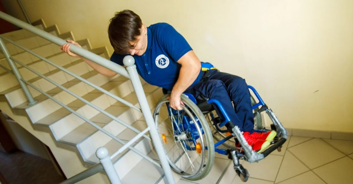 Une personne en fauteuil roulant naviguant des escaliers avec une rampe intérieure, représentant les défis d'accessibilité.