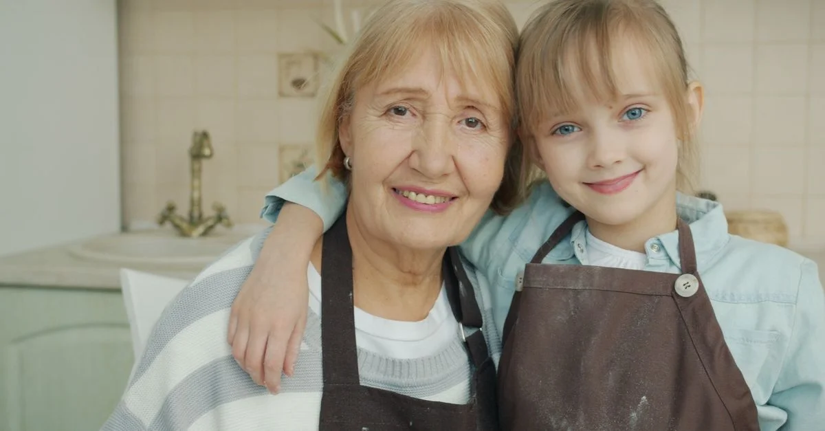 Grand-mère et petite-fille souriant dans la cuisine, portant des tabliers.