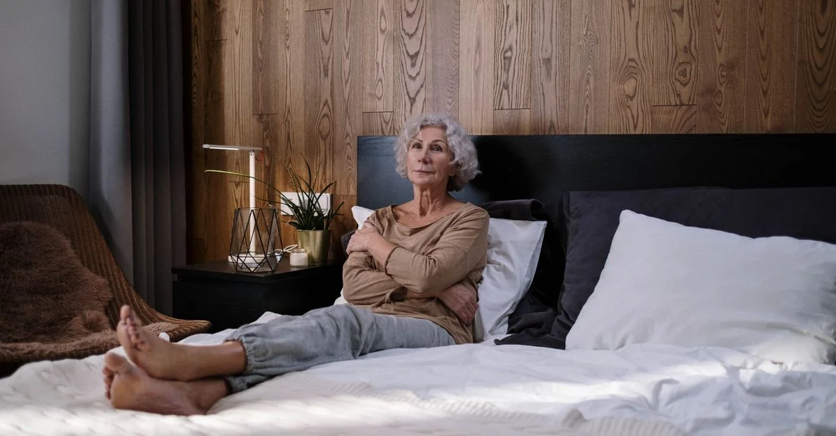 Femme âgée assise sur un lit dans un environnement de chambre paisible, reflétant la tranquillité.