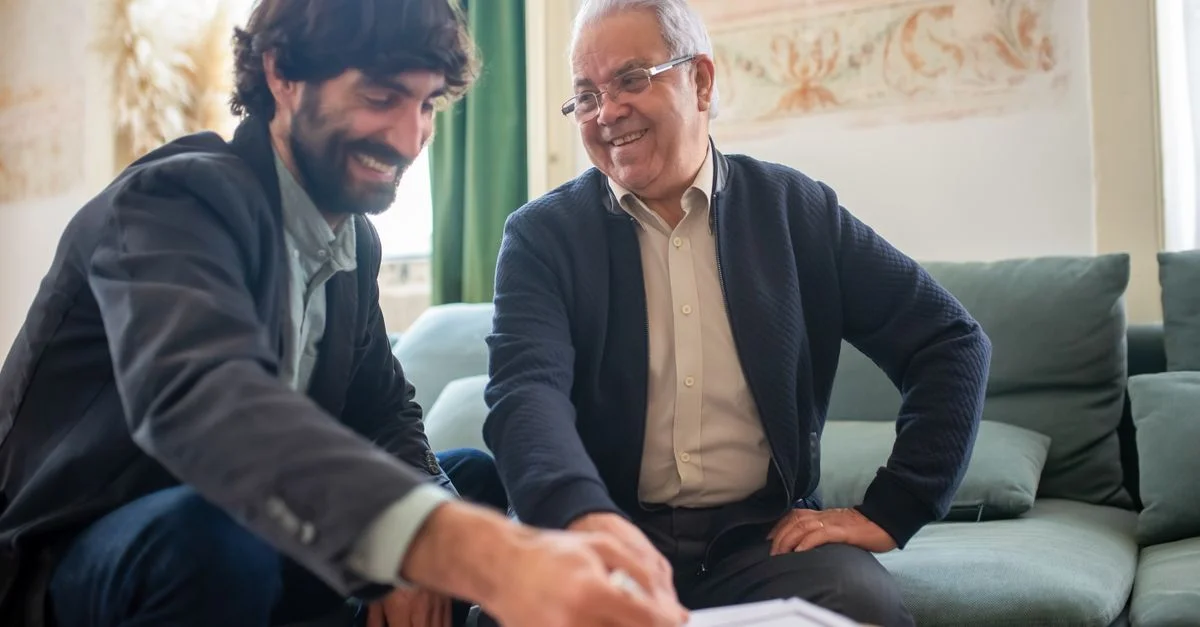 Un conseiller et un client âgé discutent de documents lors d'une session de consultation à l'intérieur.