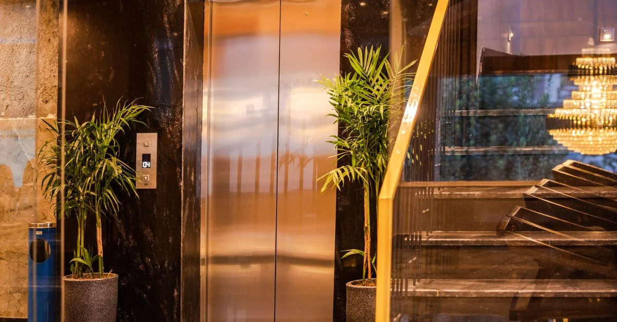 Ascenseur d'hôtel élégant avec des plantes luxuriantes et un escalier moderne, reflétant le luxe et la sophistication.