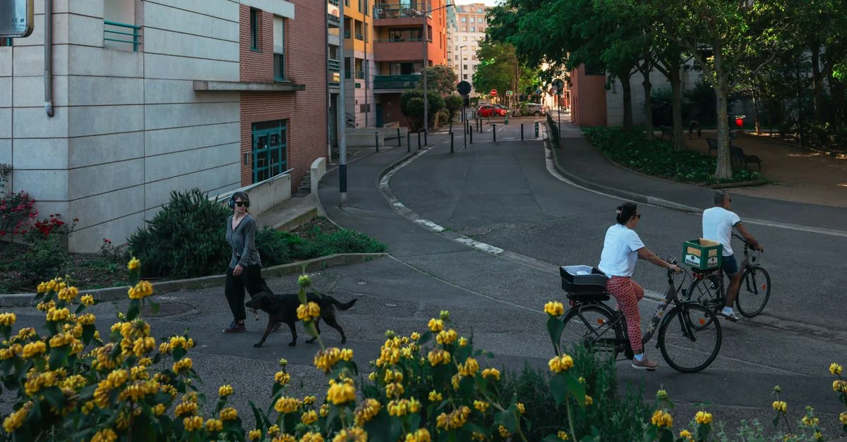 Scène de rue à Toulouse, France, mettant en vedette des cyclistes, un piéton, des bâtiments et de la flore.