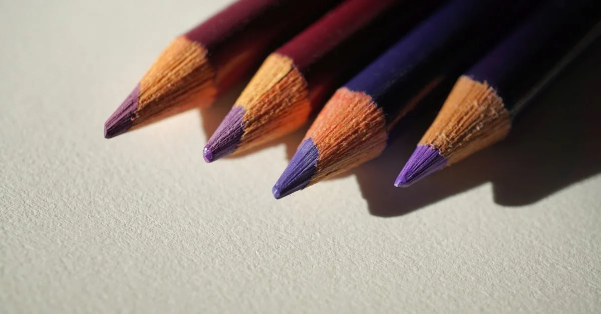 Quatre crayons de couleur violette disposés sur une surface de papier texturée.