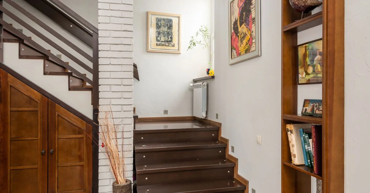Intérieur chaleureux avec un escalier moderne, une bibliothèque et des éléments de décoration artistique.