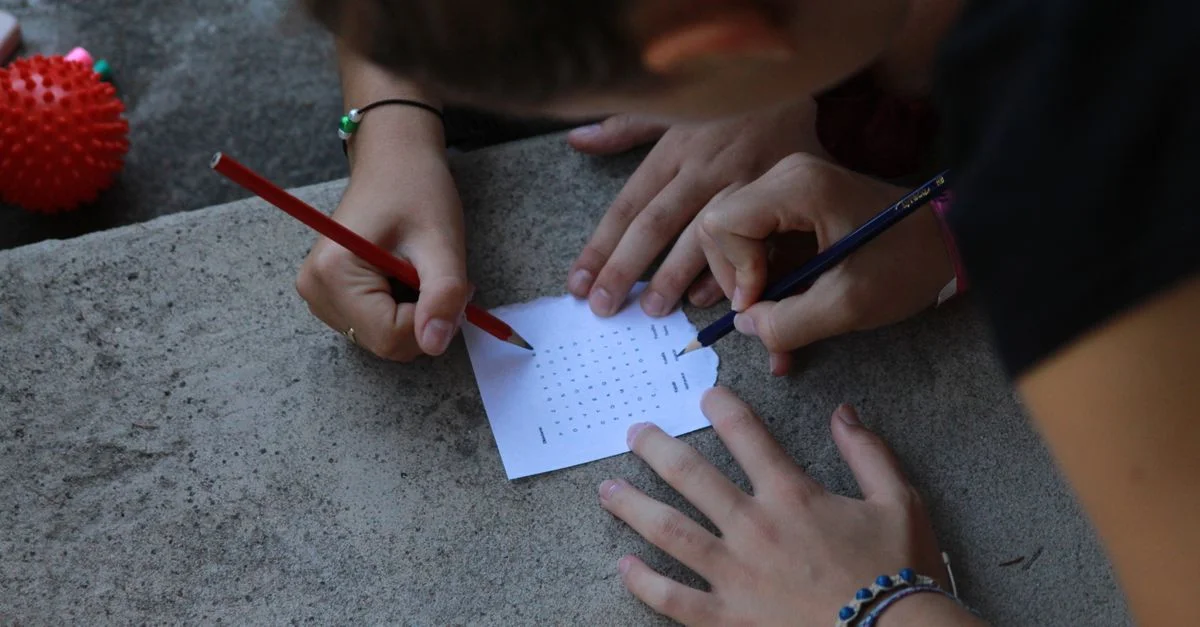 Gros plan sur des mains résolvant un mot croisé en plein air avec des crayons sur du papier.