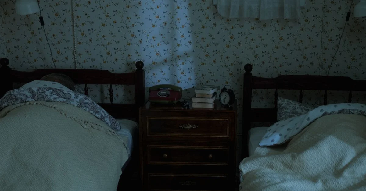 Une chambre vintage avec deux personnes endormies sous un éclairage tamisé, créant une ambiance nocturne tranquille.