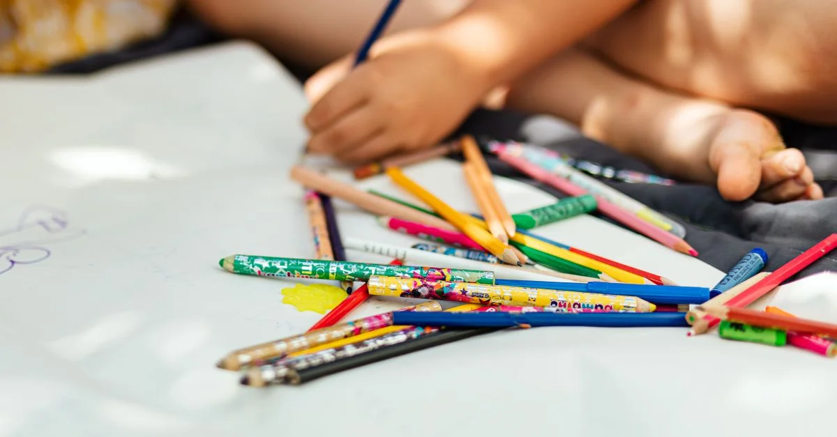 Une enfant dessinant de manière créative sur du papier avec des crayons colorés, capturant un moment artistique.