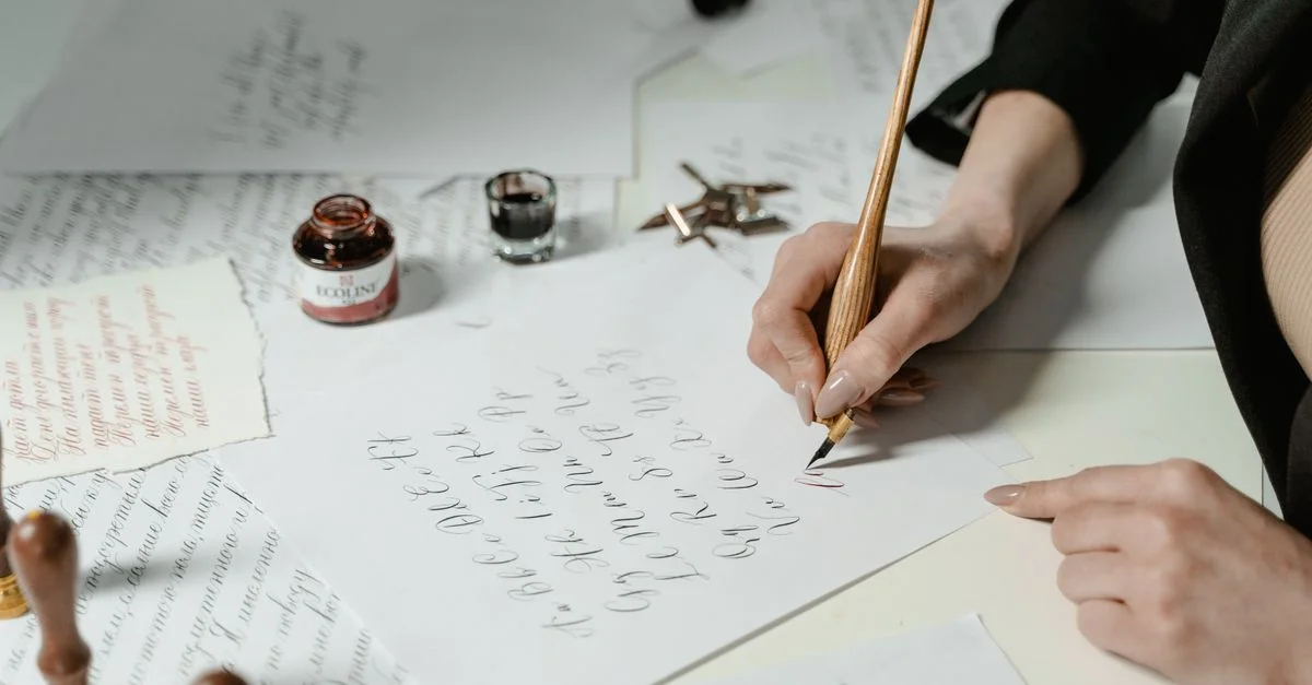 Gros plan sur un adulte écrivant de la calligraphie avec un stylo plume sur une table.